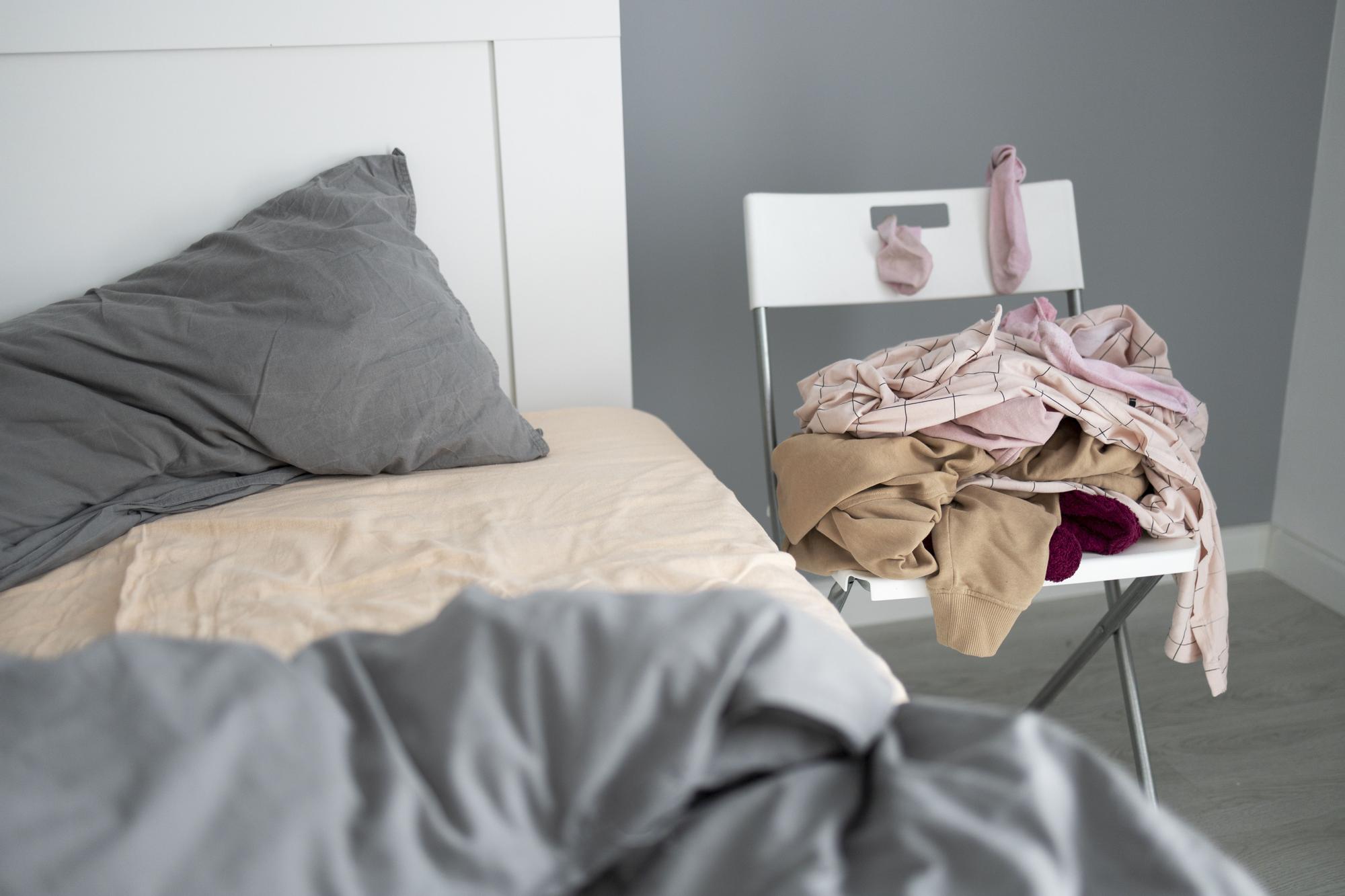 Dormitorio desordenado con ropa encima de una silla.