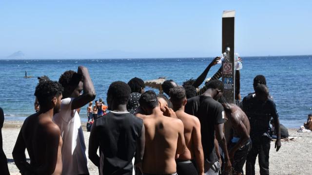 Varios migrantes hacen cola en una playa de Ceuta para ducharse y coger agua.