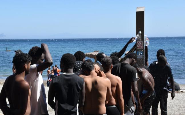 Varios migrantes hacen cola en una playa de Ceuta para ducharse y coger agua.