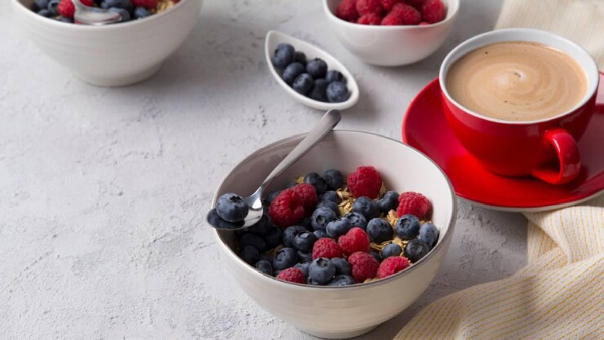 Desayuno saludable de avena con arándanos y frambuesas acompañado de un café con leche