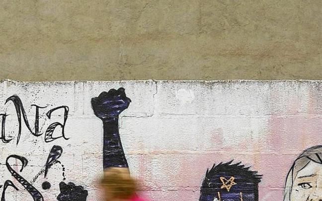 Una mujer camina frente a una pintada feminista.