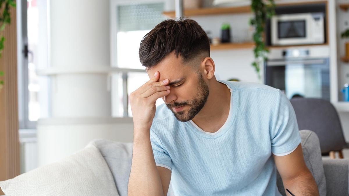Un hombre con dolor de cabeza se lleva la mano a la frente.