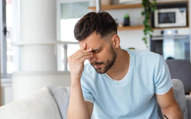 Un hombre con dolor de cabeza se lleva la mano a la frente.