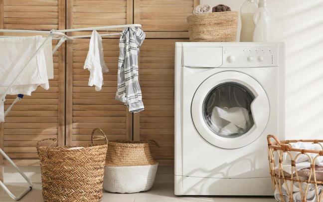 Una lavadora, junto a un tendedor y varios cestos con ropa.