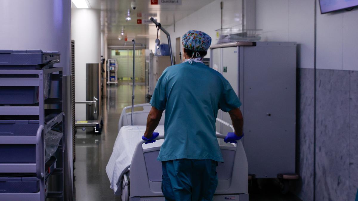 Un celador transporta una camilla vacía en un hospital.