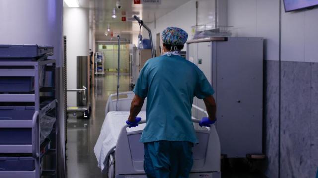 Un celador transporta una camilla vacía en un hospital.