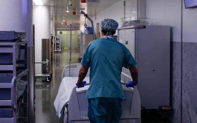 Un celador transporta una camilla vacía en un hospital.