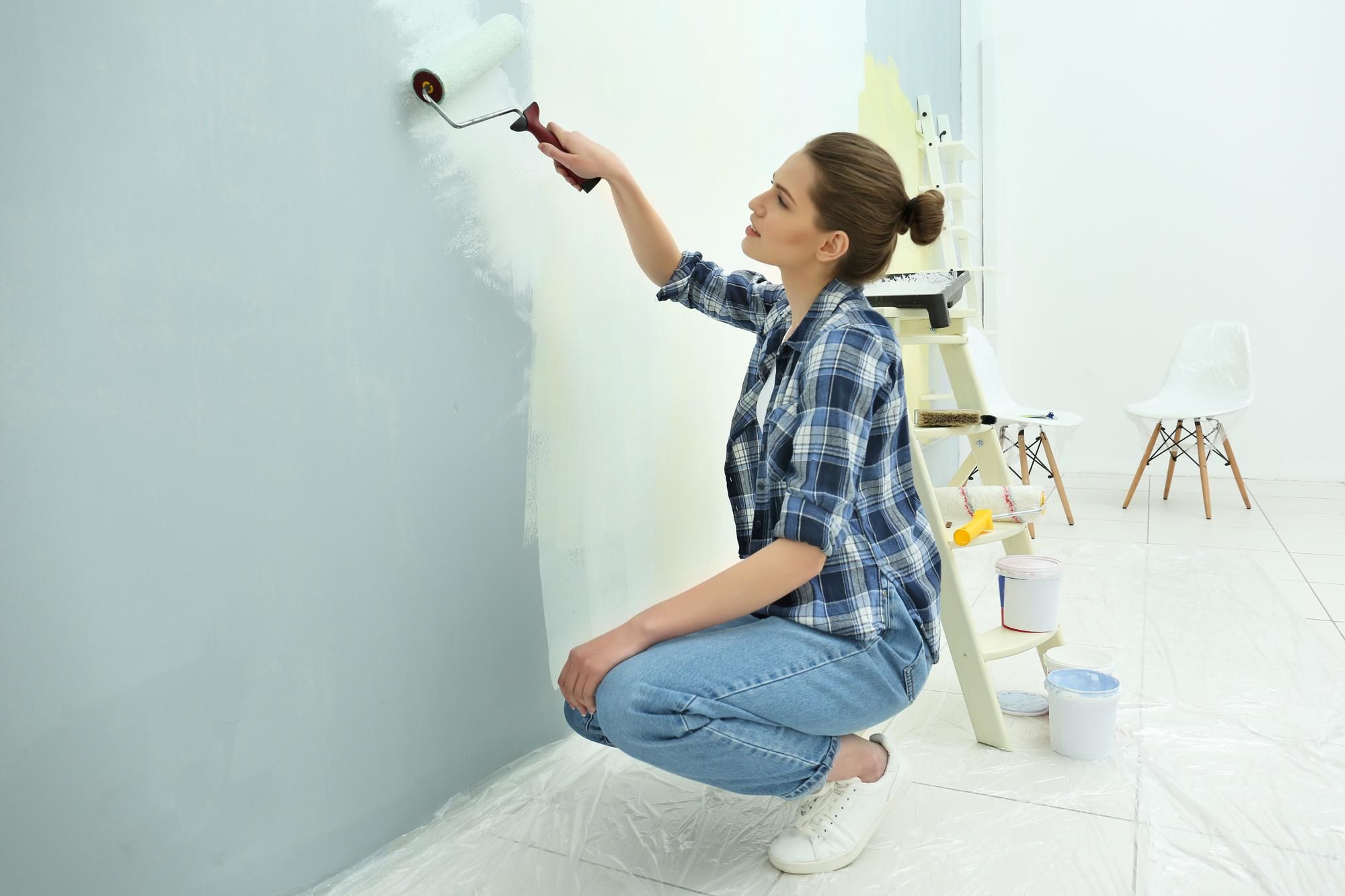 Una mujer pinta una pared en color gris.