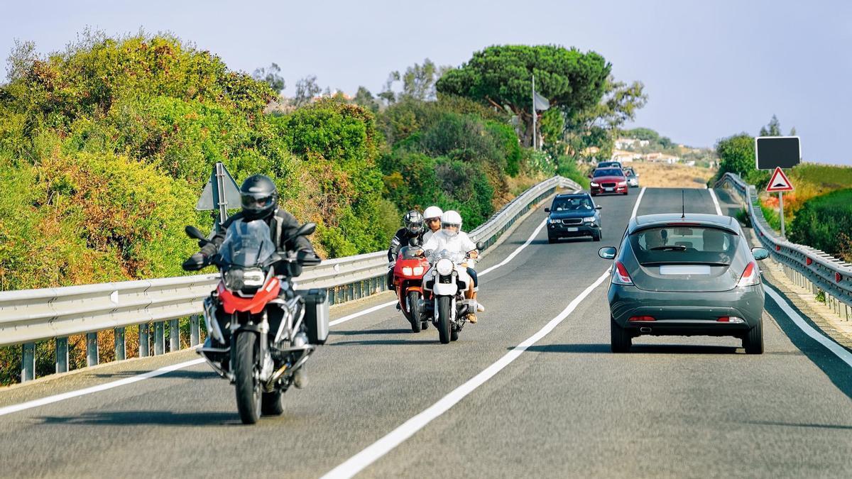 Varias motos circulan junto a otros vehículos por una carretera de doble sentido.