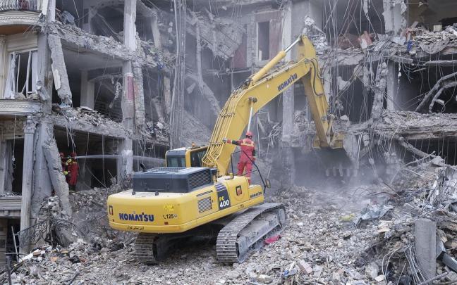 Unos trabajadores desescombran con una excavadora un edificio atacado por EE.UU. e Israel en el barrio de Andarzgu, en el noreste de Teherán