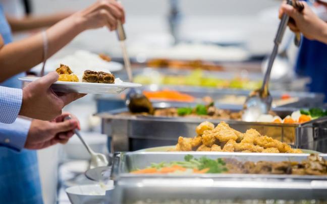 Unas personas se sirven comida en un buffet libre.