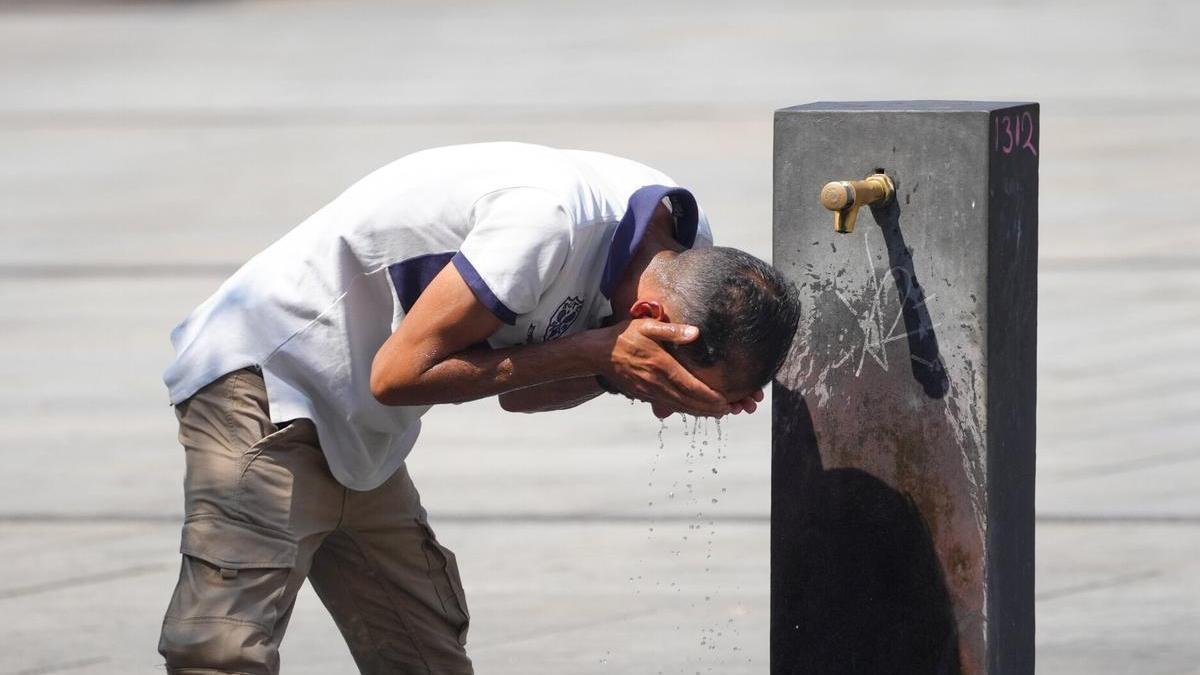 Un hombre refrescándose en una fuente durante un ola de calor.