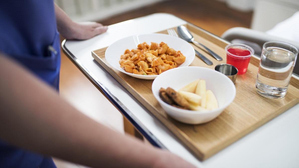 Una sanitaria lleva a un paciente una bandeja de comida en un hospital.