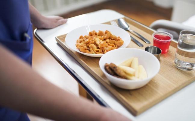Una sanitaria lleva a un paciente una bandeja de comida en un hospital.