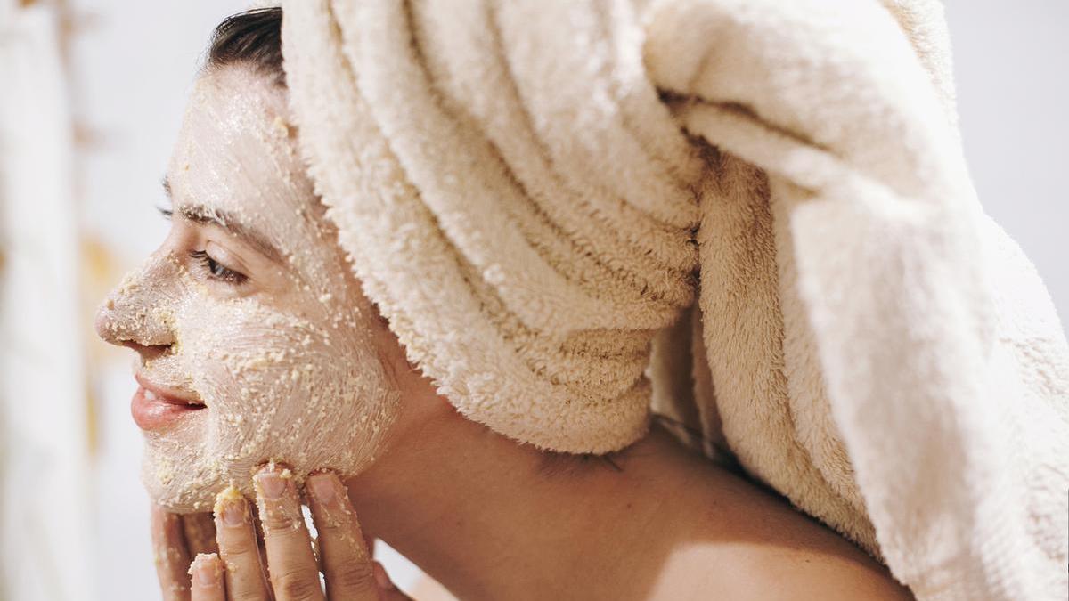 Chica se realiza una exfoliación facial frente al espejo nada más salir de la ducha.