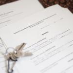 Unas llaves sobre un contrato de compraventa de vivienda y un contrato de arrendamiento (alquiler) de una habitación en una vivienda.
