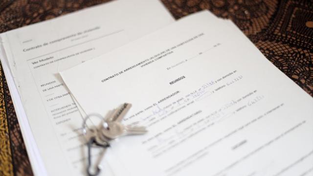 Unas llaves sobre un contrato de compraventa de vivienda y un contrato de arrendamiento (alquiler) de una habitación en una vivienda.