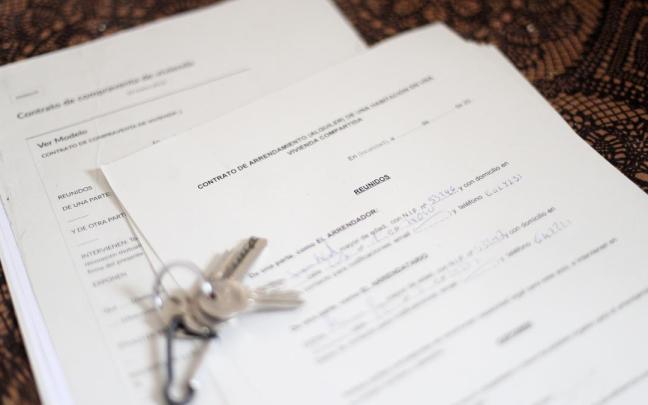 Unas llaves sobre un contrato de compraventa de vivienda y un contrato de arrendamiento (alquiler) de una habitación en una vivienda.