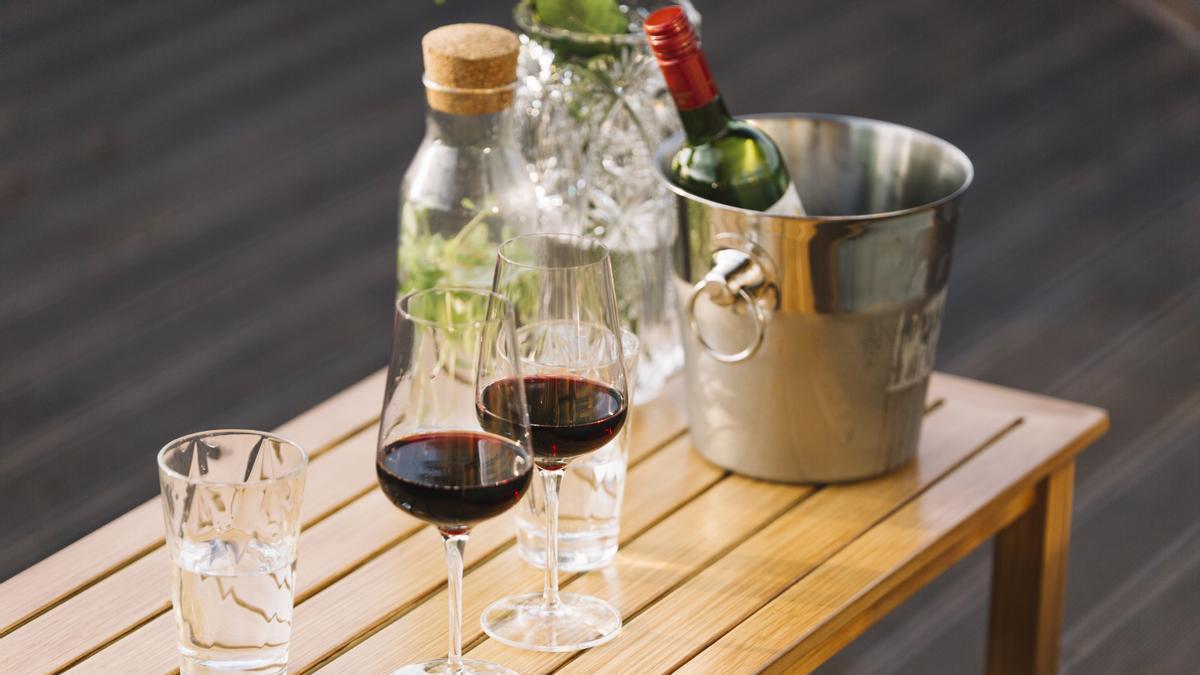 Botella de vino tinto en una cubitera con dos copas sobre una mesa de madera