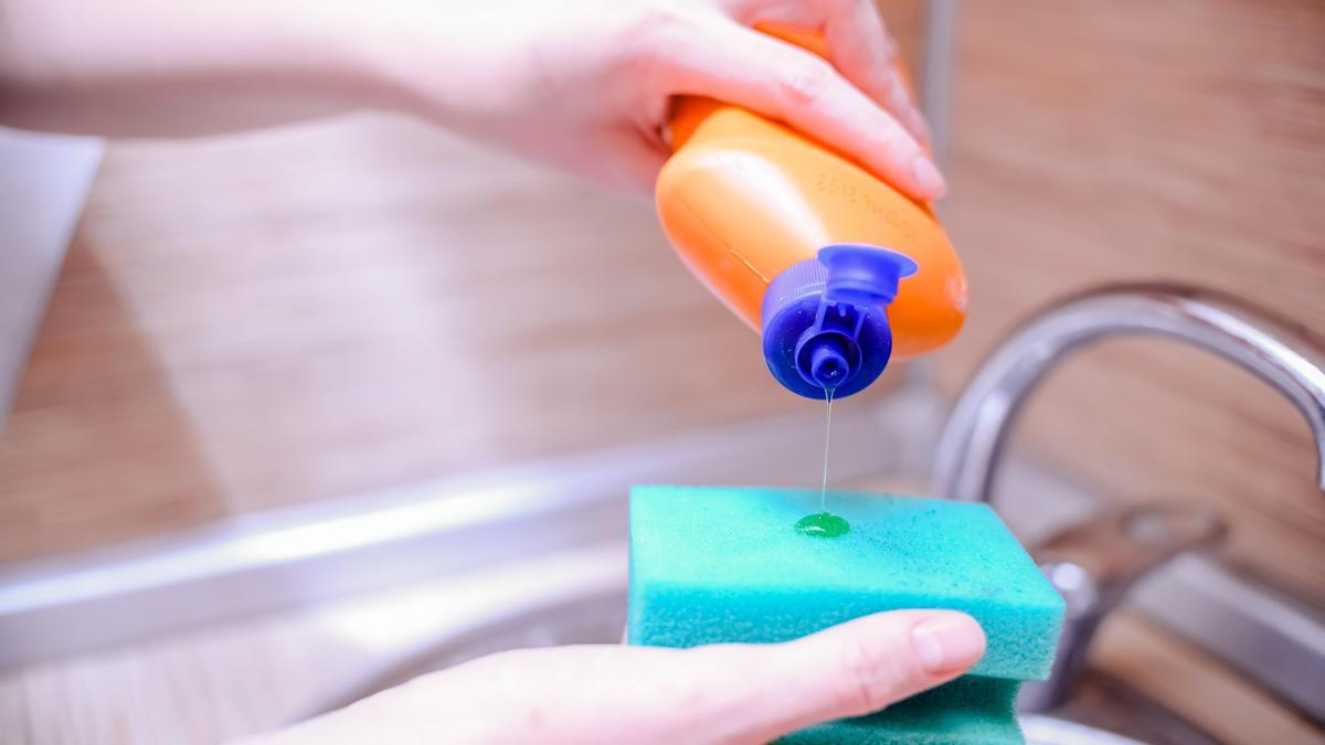 Una mujer vierte un chorro de jabón de fregar en un estropajo.