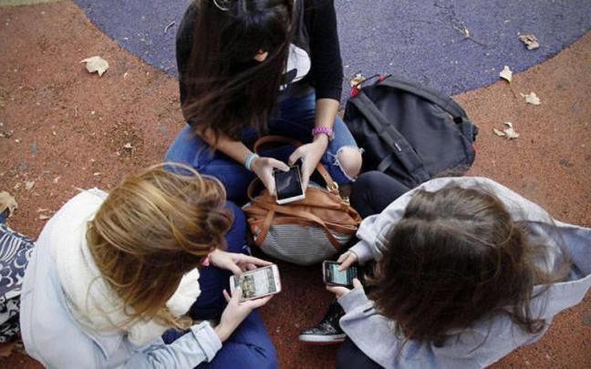 Un grupo de menores usando sus teléfonos móviles en un parque.