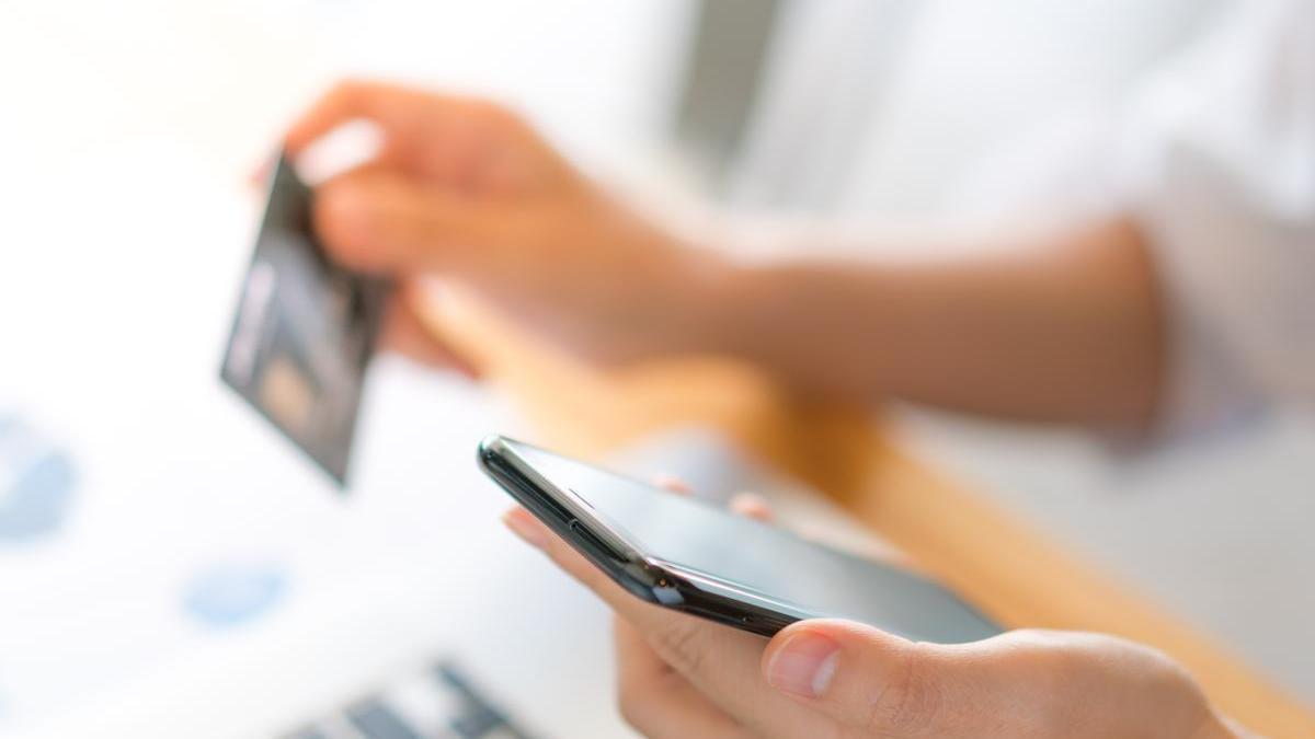 Una joven sostiene su teléfono móvil en una mano y su tarjeta de crédito en la otra mientras completa una transacción