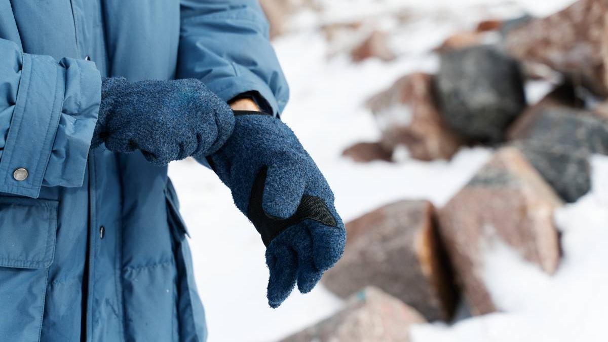 Manos de un hombre con un abrigo azul poniéndose guantes para protegerse del frío en la nieve