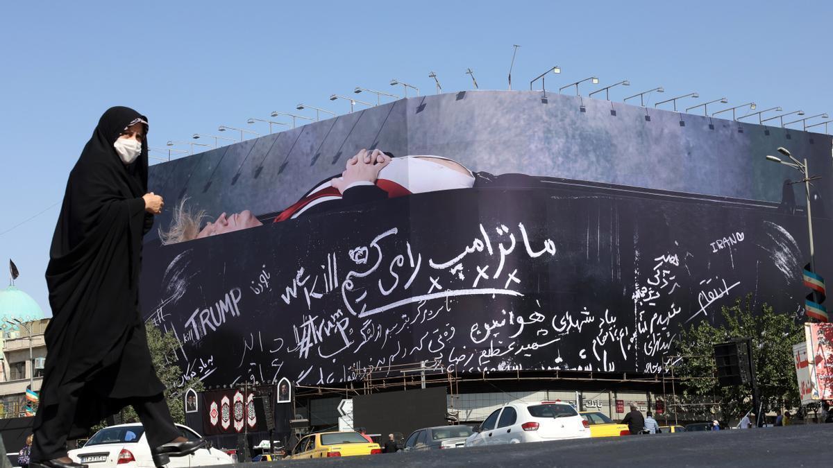 Una mujer iraní camina ante un cartel en Teherán que muestra a Donald Trump en un ataúd.