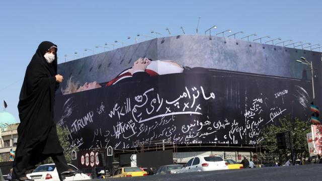 Una mujer iraní camina ante un cartel en Teherán que muestra a Donald Trump en un ataúd.