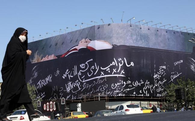 Una mujer iraní camina ante un cartel en Teherán que muestra a Donald Trump en un ataúd.