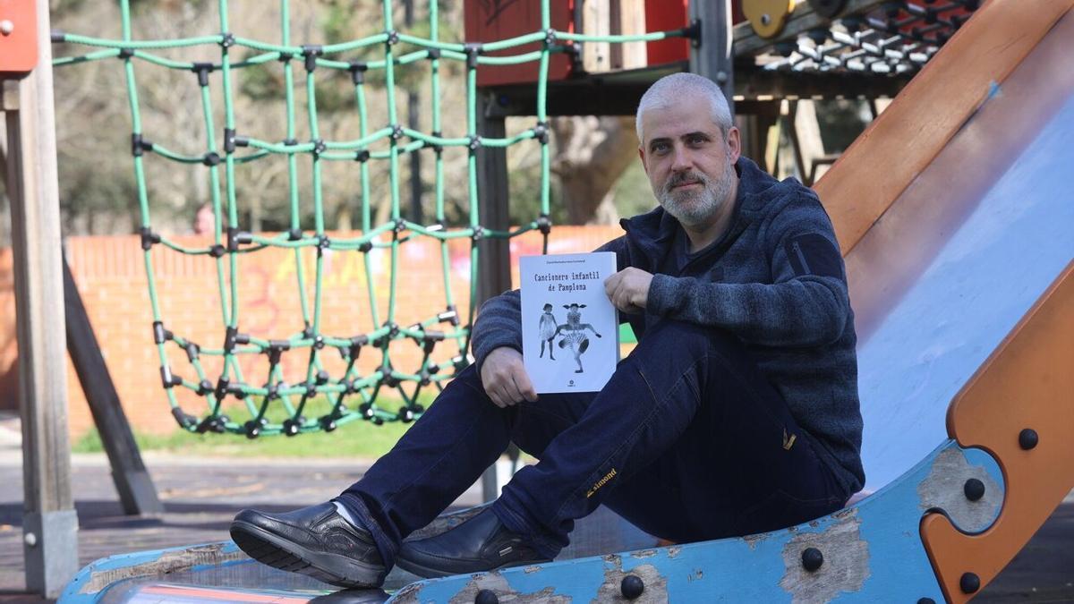 David Marriezkurrena, sentado en un tobogán, posa con su libro 'Cancionero Infantil de Pamplona'.