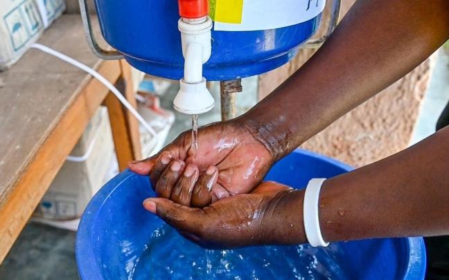 Una persona se lava las manos en un dispensador con una solución clorada al 0.05%, instalada en una comunidad de RDC para fomentar la higiene de manos y prevenir el cólera.