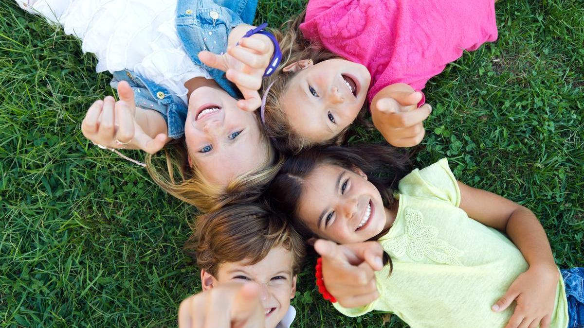 Niños juegan en el parque tumbados en la hierba con una sonrisa en la cara.