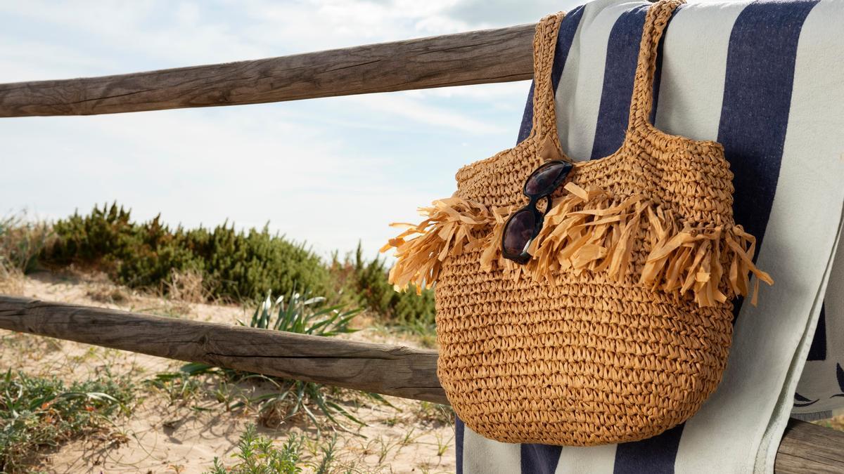 Toalla y bolso colgados en una barandilla de madera en la playa.