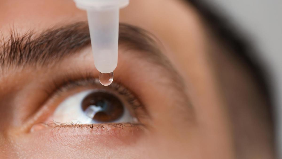 Un hombre se echa una gota de colirio en el ojo.