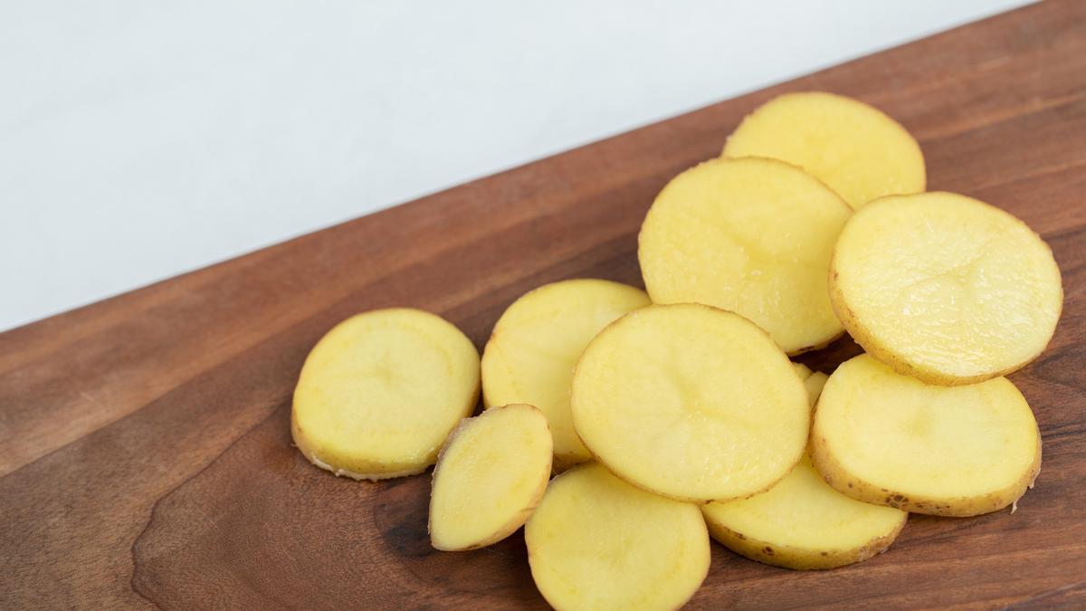 Una patata cortada en rodajas sobre una superficie de madera.