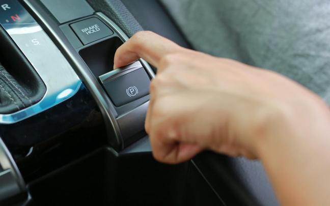 Una persona acciona el freno de mano eléctrico de su coche.