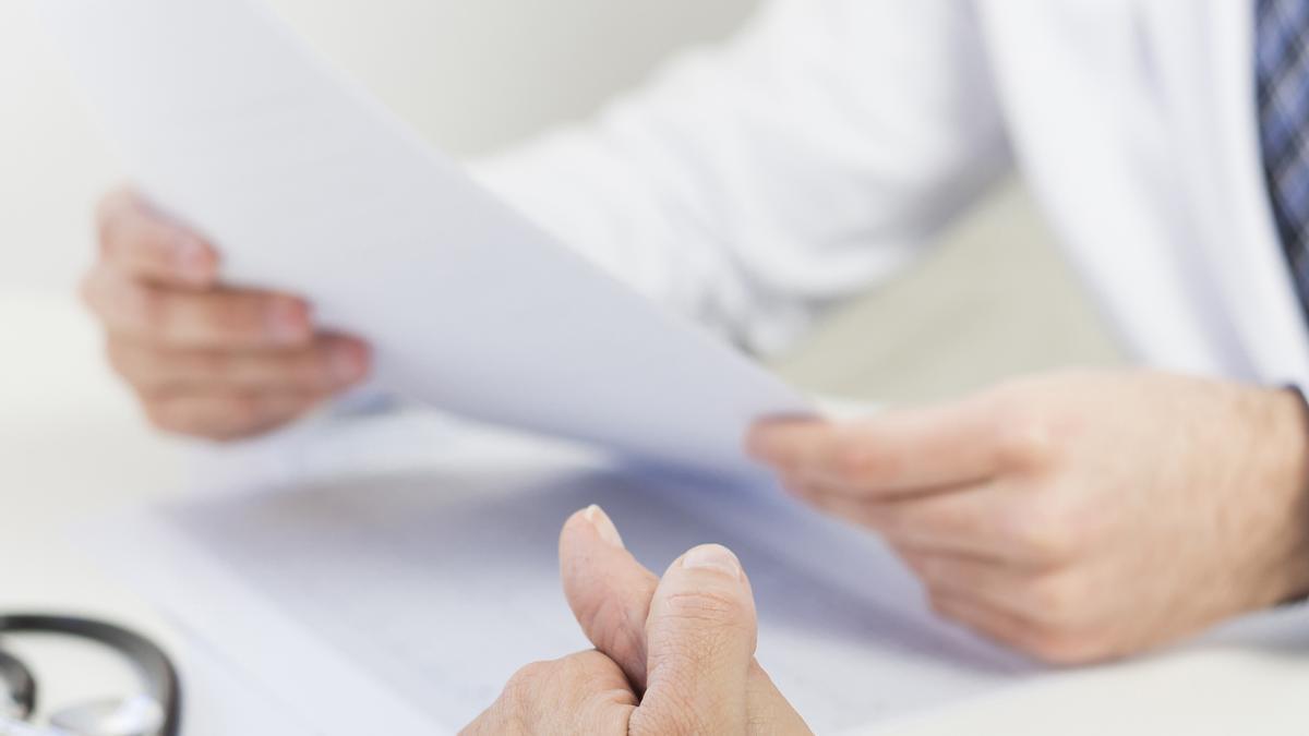 Un médico de cabecera mirando la historia de un paciente en consulta.