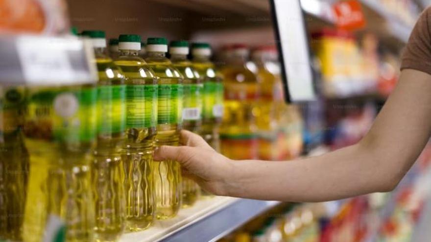 Una persona cogiendo una botella de aceite en un supermercado