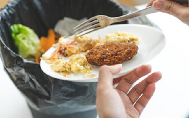 Una persona tira una ración de comida al cubo de la basura. Una persona tira una ración de comida al cubo de la basura.