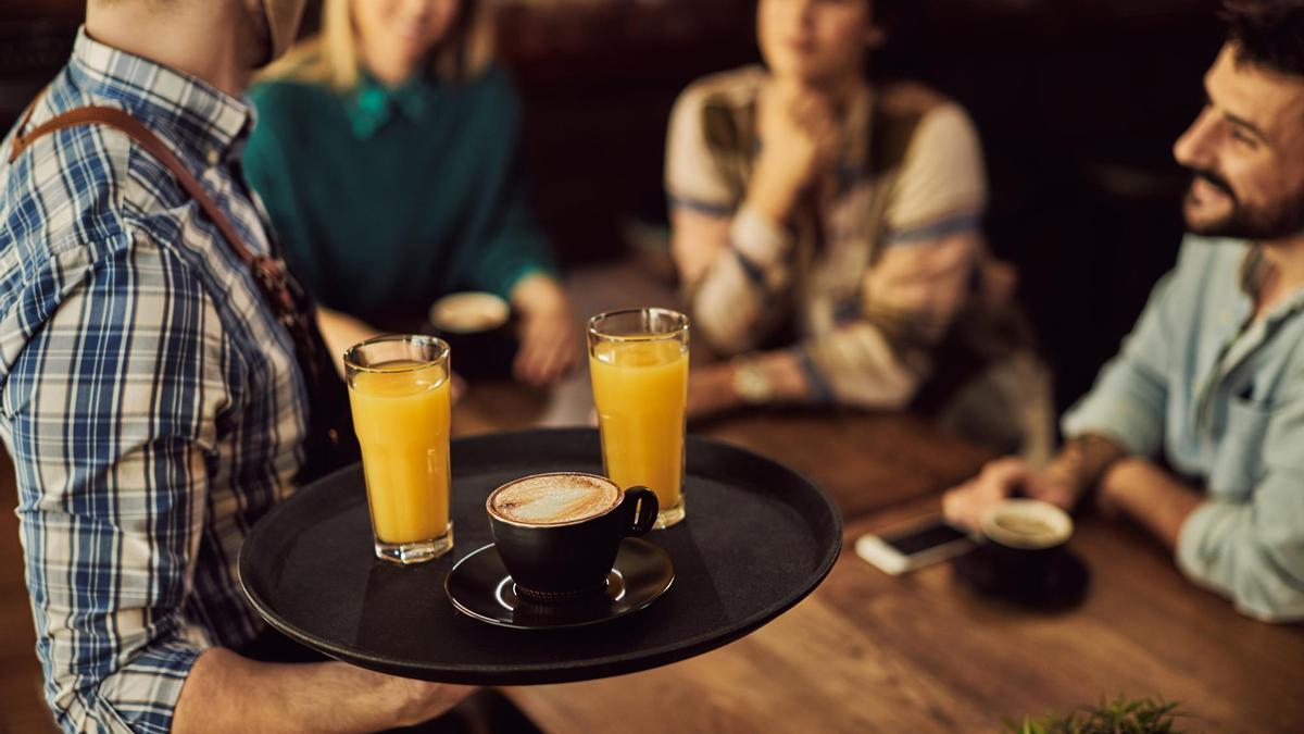 Un camarero sirve sus consumiciones a tres clientes en un bar.