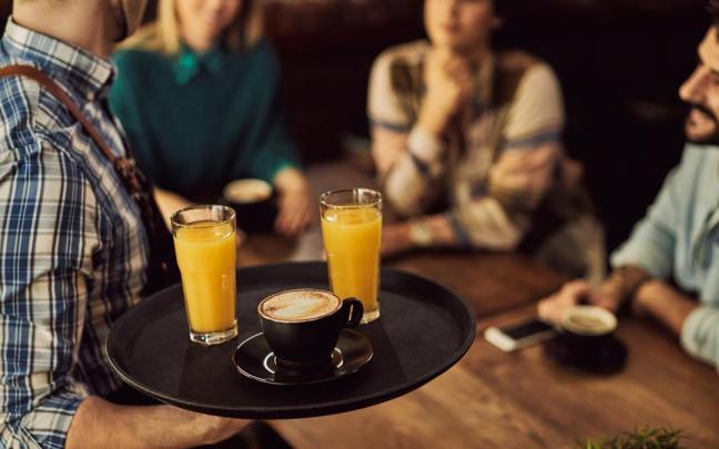 Un camarero sirve sus consumiciones a tres clientes en un bar.