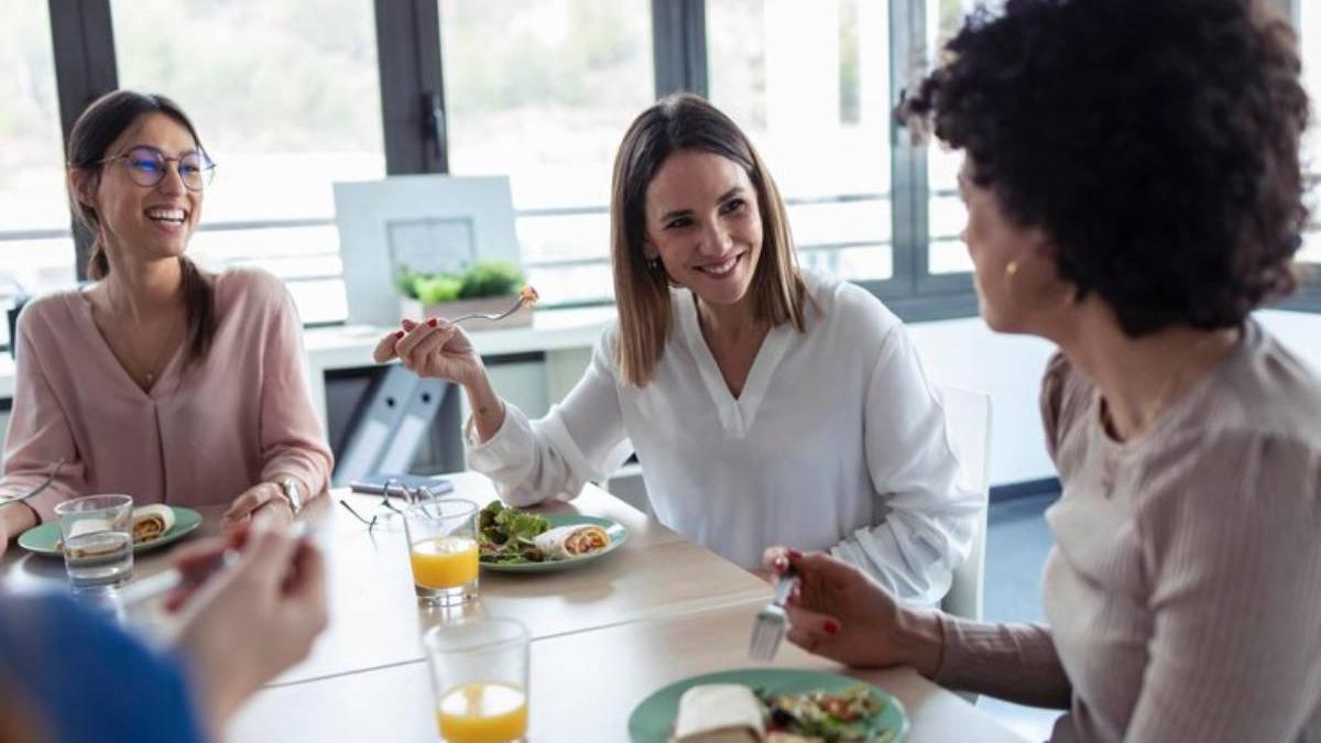 Compañeras comen juntas y disfrutan de una conversación agradable durante su pausa para la comida en el trabajo.