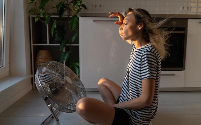 Una mujer se refresca con un ventilador en su casa.