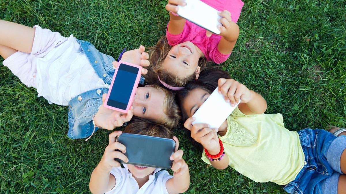 Un grupo de niños se hace una foto y juega con sus teléfonos móviles mientras están tumbados un parque.