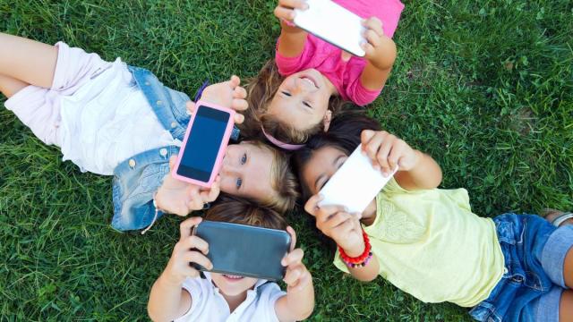 Un grupo de niños se hace una foto y juega con sus teléfonos móviles mientras están tumbados un parque.