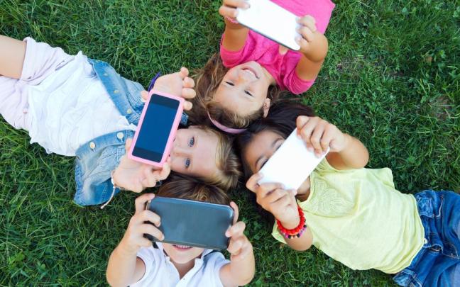 Un grupo de niños se hace una foto y juega con sus teléfonos móviles mientras están tumbados un parque.