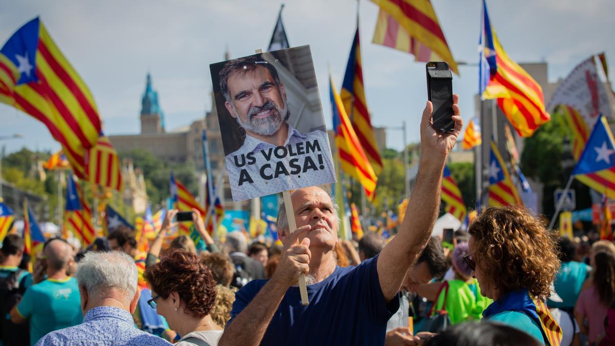 Un hombre sujeta un cartel con la foto del preso del Procés y Presidente de Òmnium Cultural, Joredi Cuixart, en la que se lee `Us Volem,a casa´(os queremos en casa) junto con banderas de la estelada.