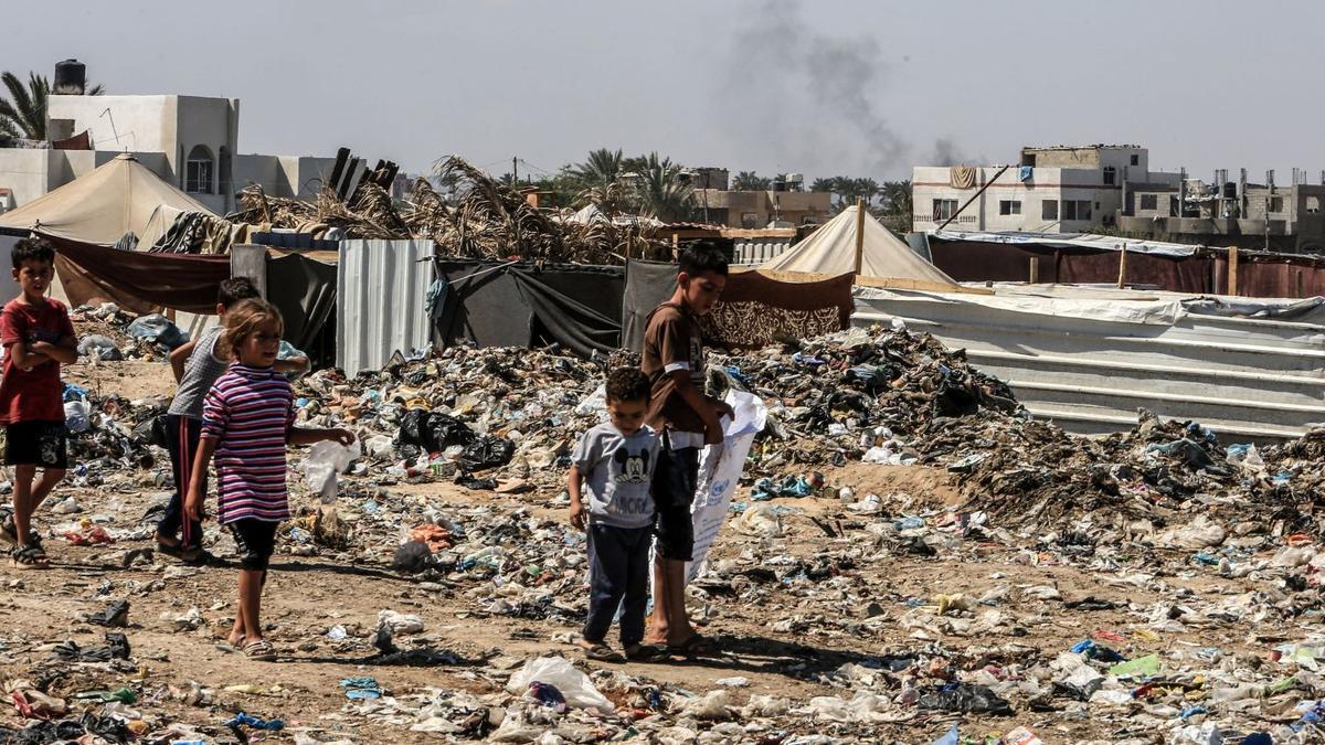 Unos niños caminan entre la basura en un campo de refugiados de la Franja de Gaza tras los continuos ataques israelíes.