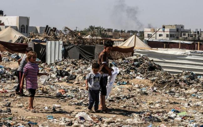 Unos niños caminan entre la basura en un campo de refugiados de la Franja de Gaza tras los continuos ataques israelíes.